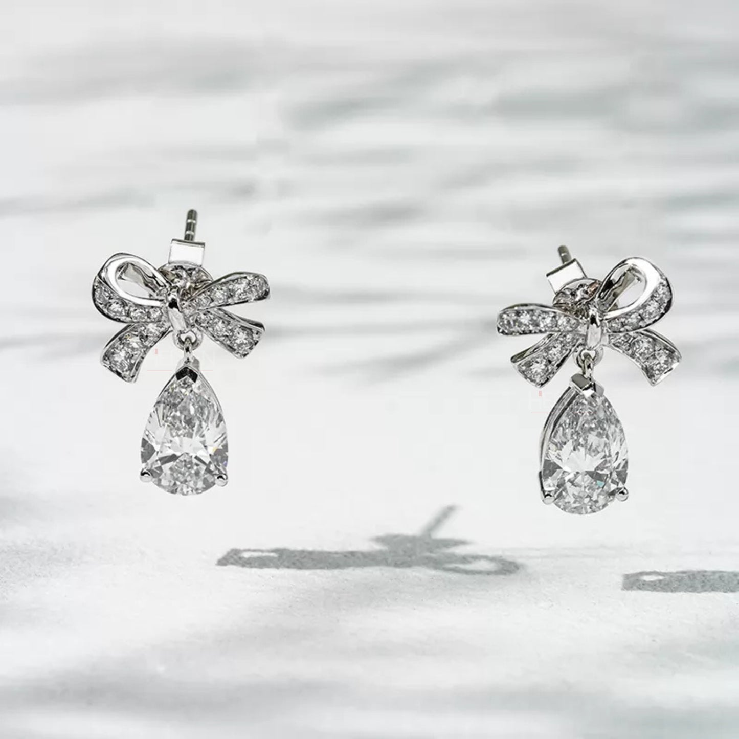 Pear cut moissanite drop earrings with elegant bow knot design in sterling silver – front view on white background